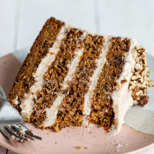 a slice of carrot cake on a plate with a fork, ready to serve.