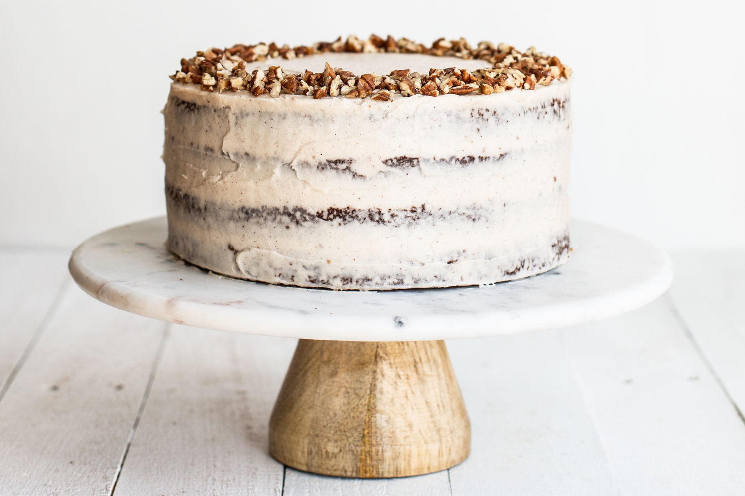 the whole frosted brown butter carrot cake, on a cake stand against a plain white background.