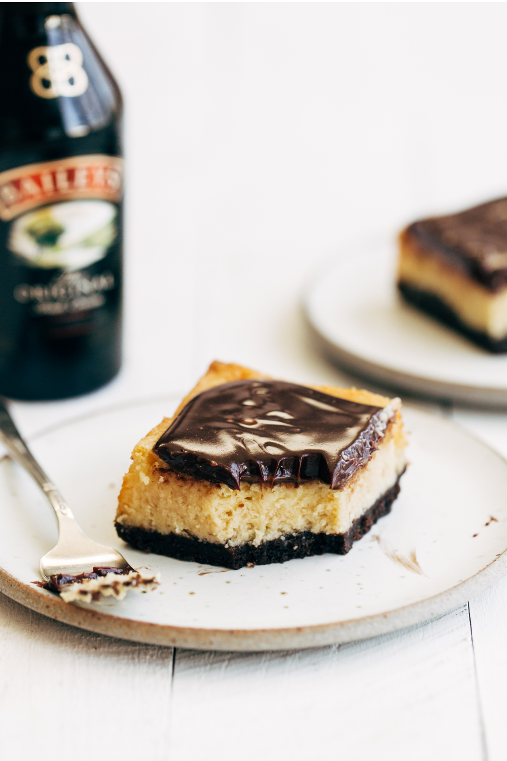 a bottle of Bailey's Irish Cream behind a couple slices of cheesecake bars on plates, ready to serve.