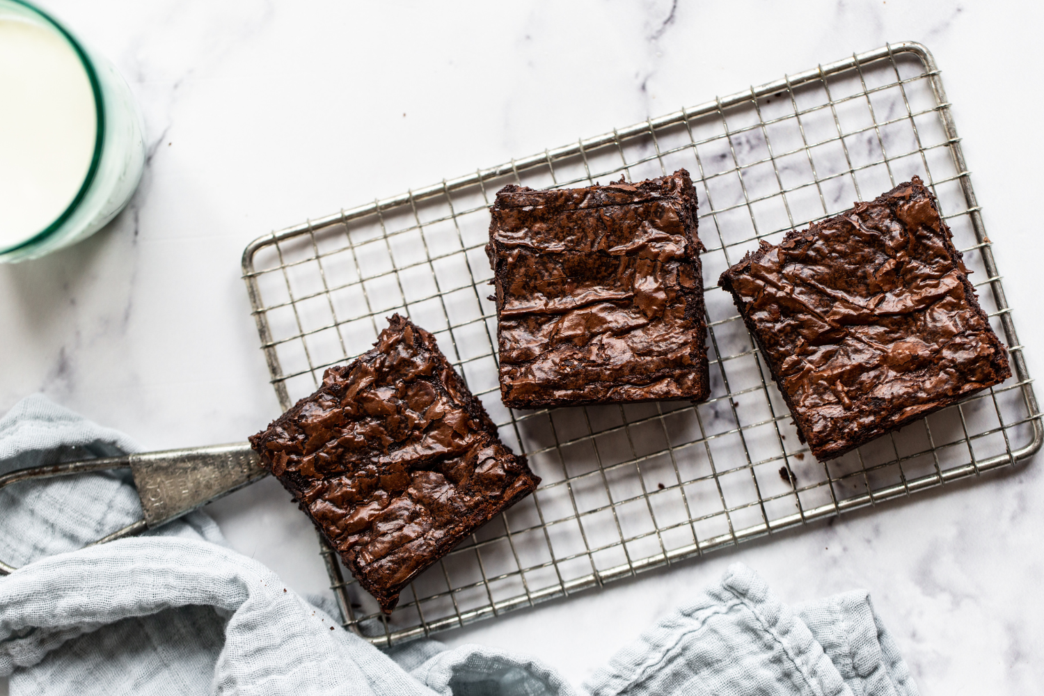 brown butter brownies on a cooling rack, with a glass of milk in the background