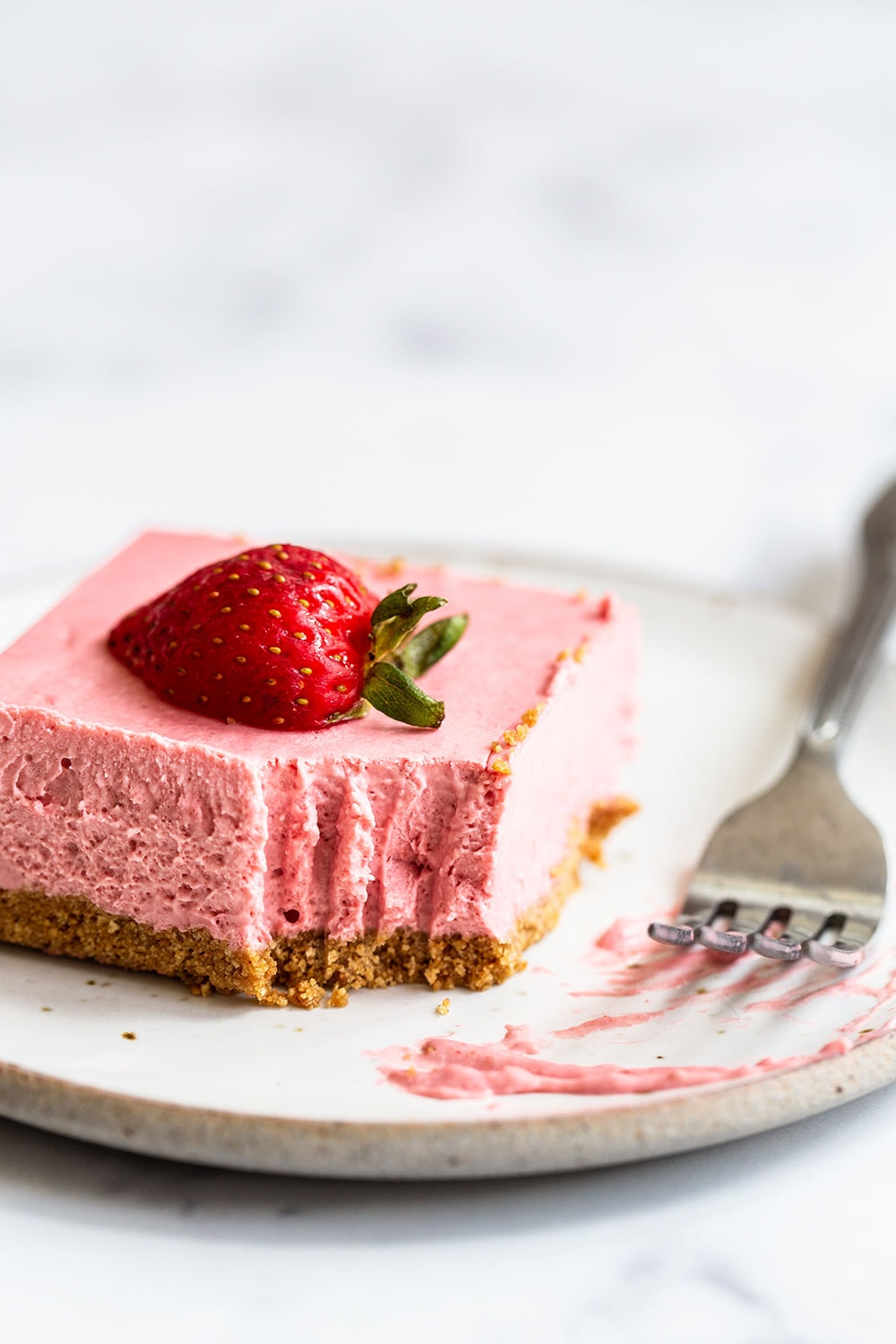 Homemade no bake strawberry cheesecake bar on a plate with a sliced strawberry on top