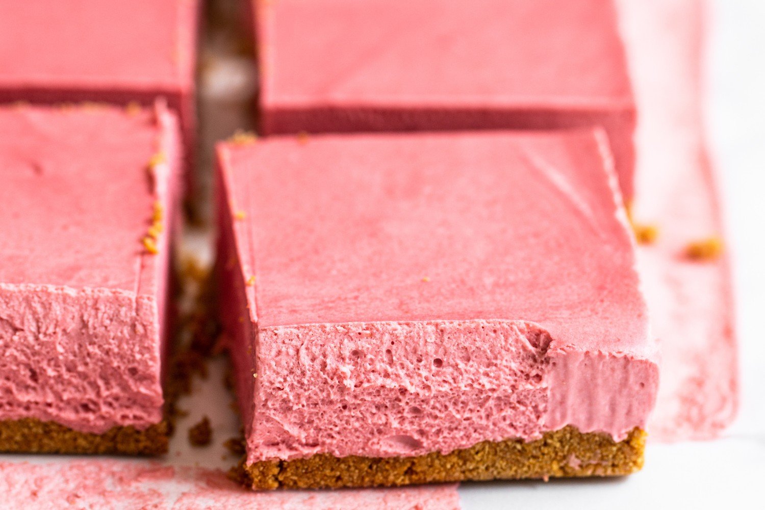 a few slices of no-bake strawberry cheesecake bars on parchment paper.