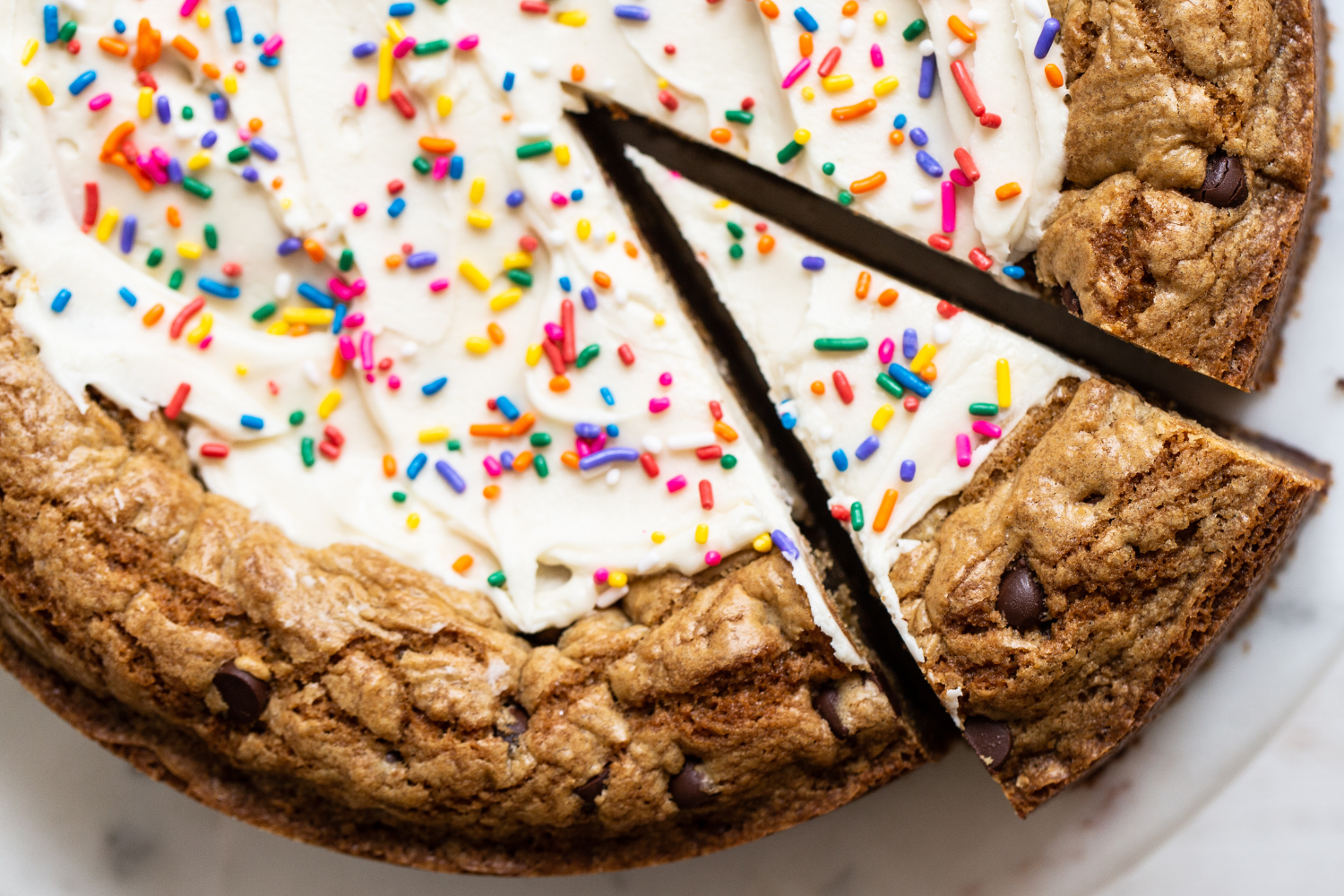 close up shot of a frosted cookie cake, with a slice being cut and removed to serve