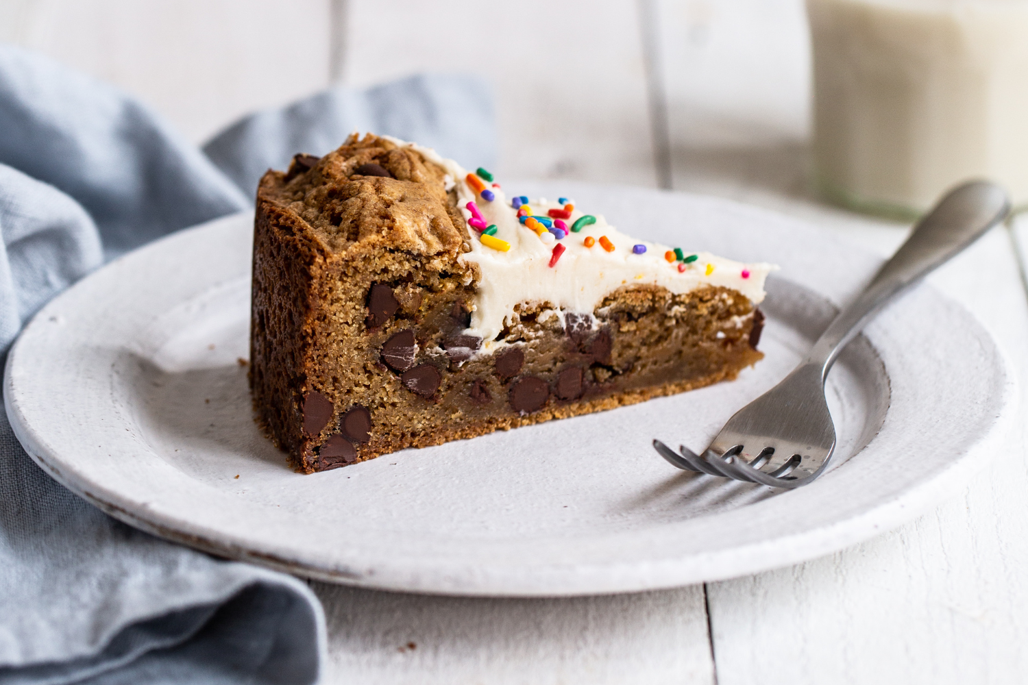 a thick, chewy slice of chocolate chip cookie cake on a plate with a fork and a napkin, ready for serving