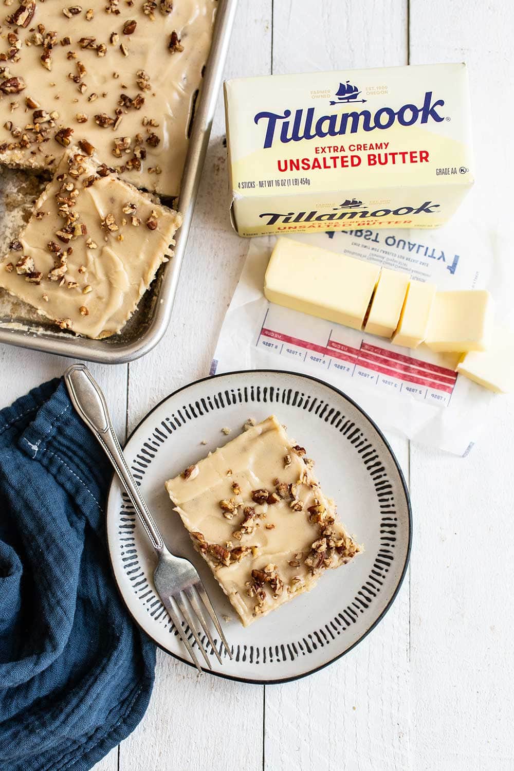 slice of butter pecan sheet cake on a plate with Tillamook butter in the background