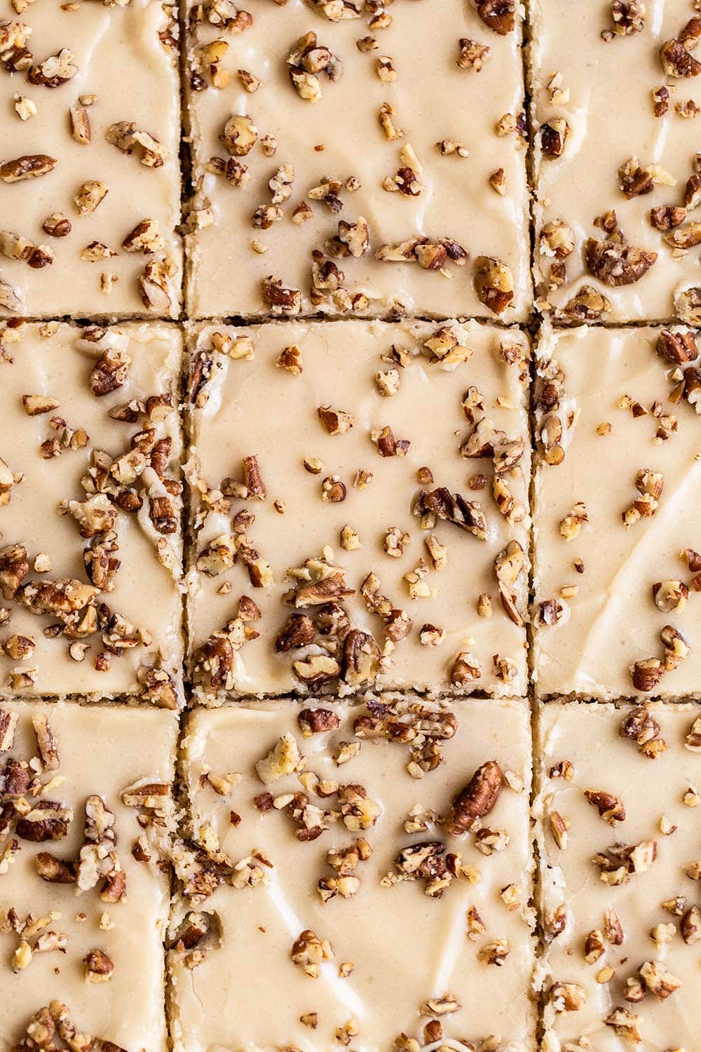 butter pecan sheet cake cut into squares with brown sugar frosting and chopped pecans on top