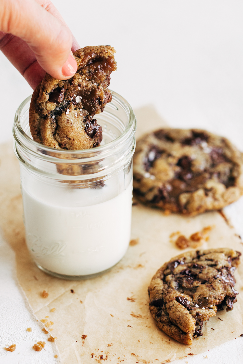 a hand dunking half a cookie into a glass of milk.