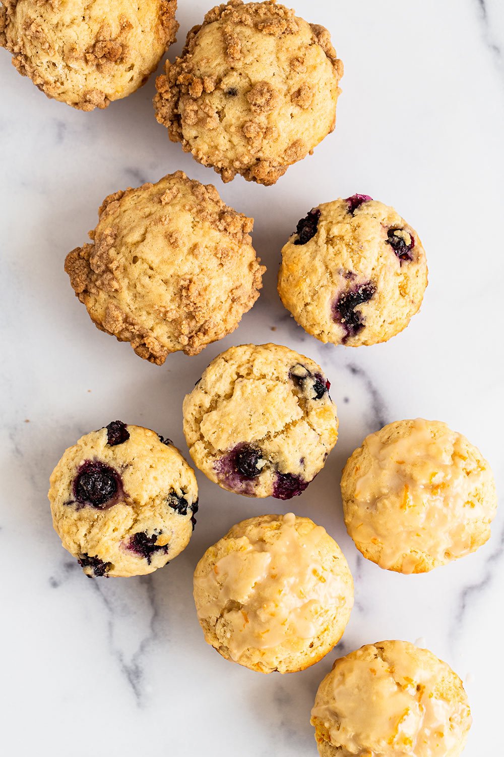 an assortment of beautiful tall bakery style muffins on a marble background.