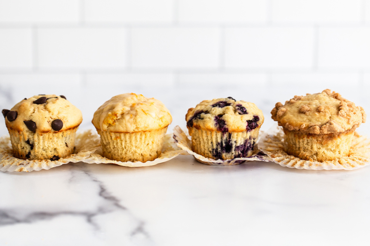 lineup of beautiful ultimate muffins in liners on a white marble surface