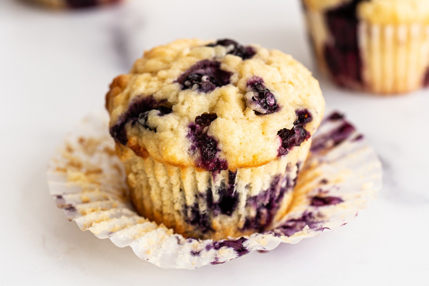 a baked blueberry muffin with the wrapper mostly removed.
