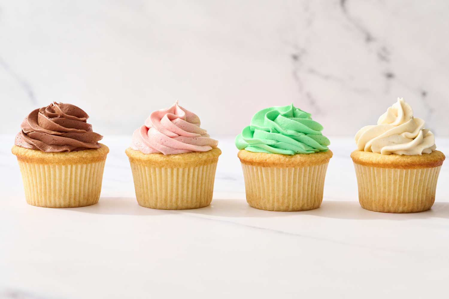 four yellow cupcakes in a row, each frosted with different flavors of buttercream frosting.