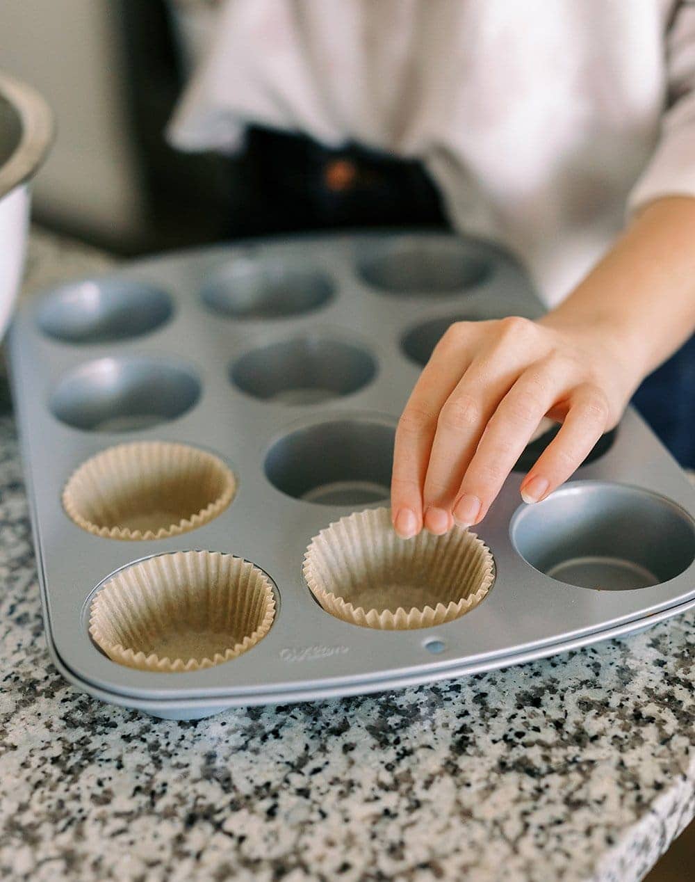 cupcake liners being placed in cupcake tin to bake cupcakes.