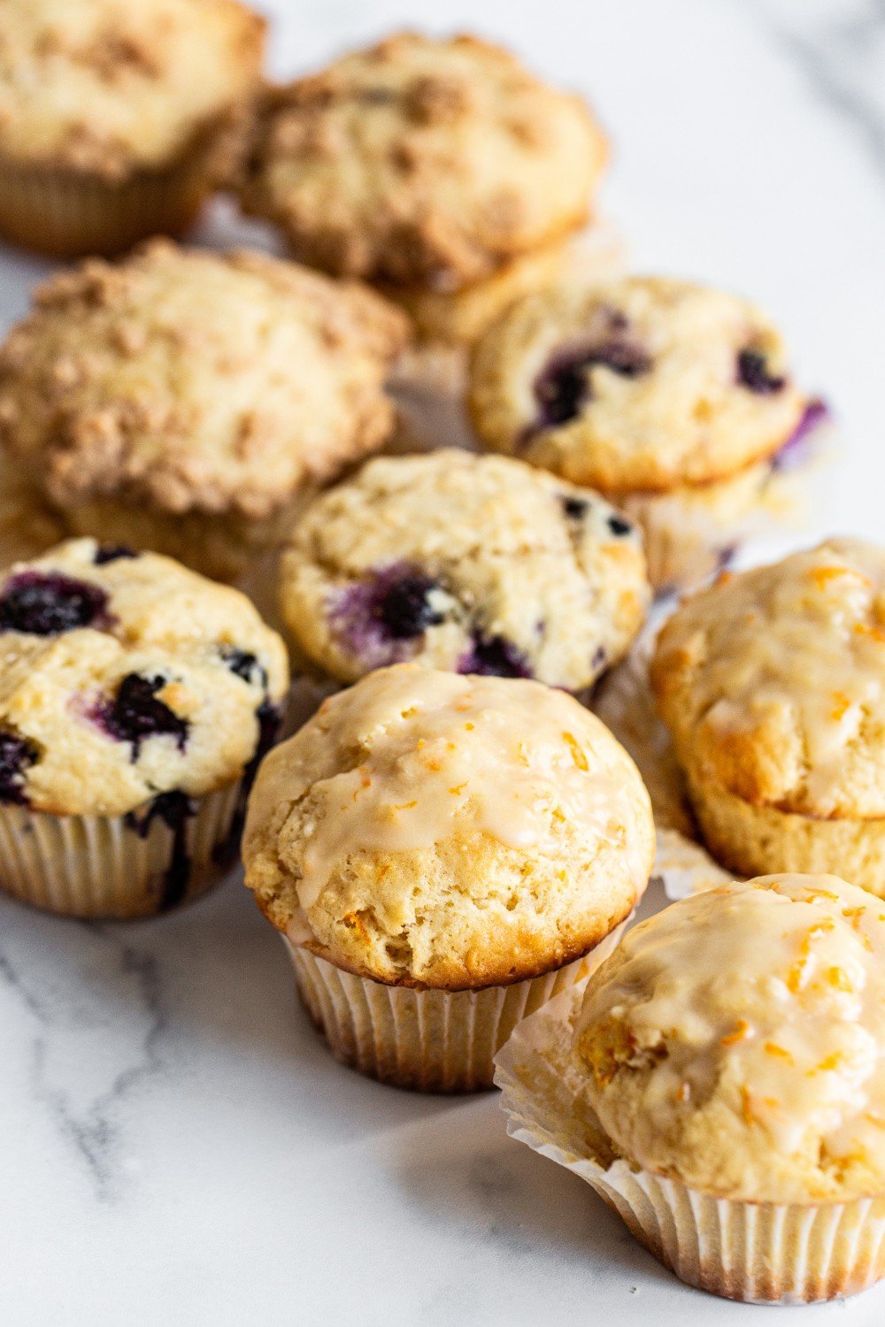 several blueberry muffins and several glazed orange muffins.