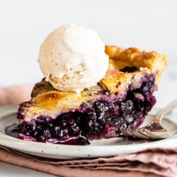 a slice of homemade blueberry pie with a scoop of vanilla ice cream on top.