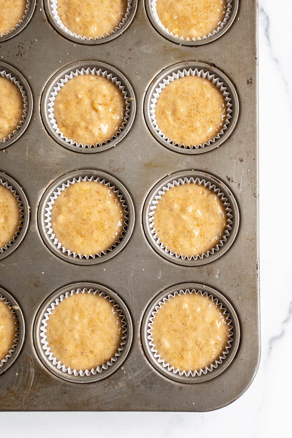 banana muffin batter divided into muffin tin cavities with liners, ready to bake