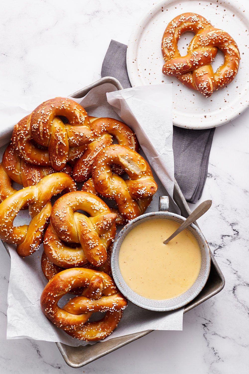 a large platter of homemade pretzels on a tray beside a bowl of beer cheese dip, ready to serve.