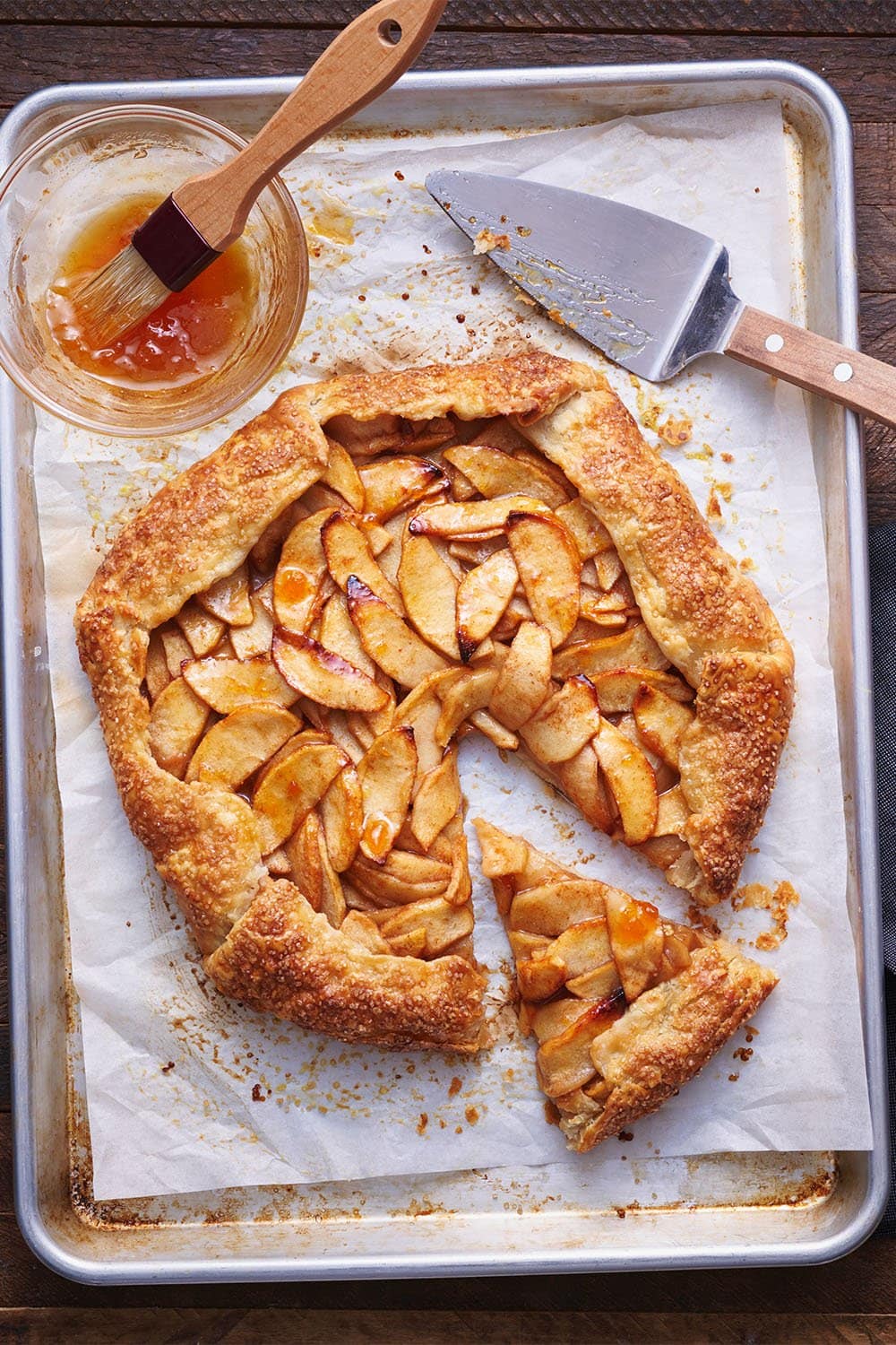 homemade rustic apple galette on a baking pan with parchment paper and apricot jam to brush on top