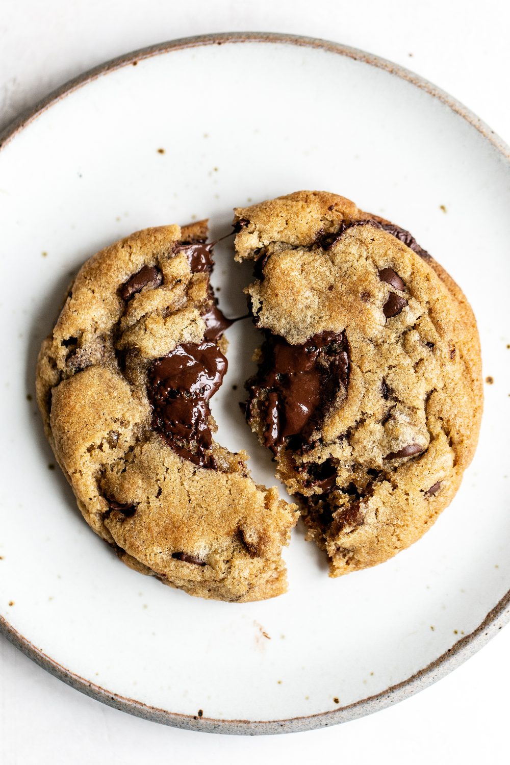a Brown Butter Chocolate Chip Cookie broken in half, sitting on a plate