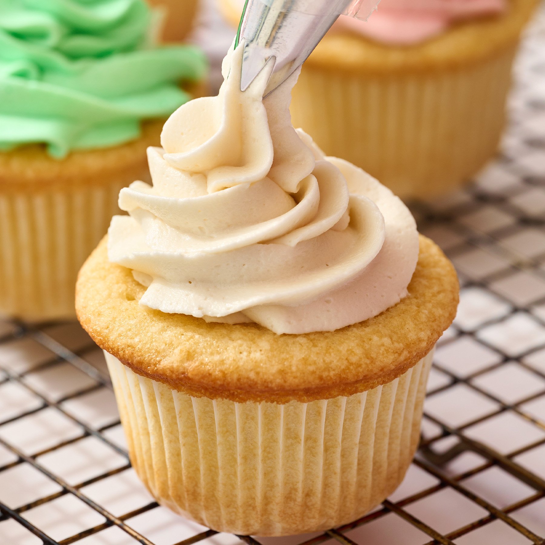 piping best buttercream recipe onto vanilla cupcake on a wire rack