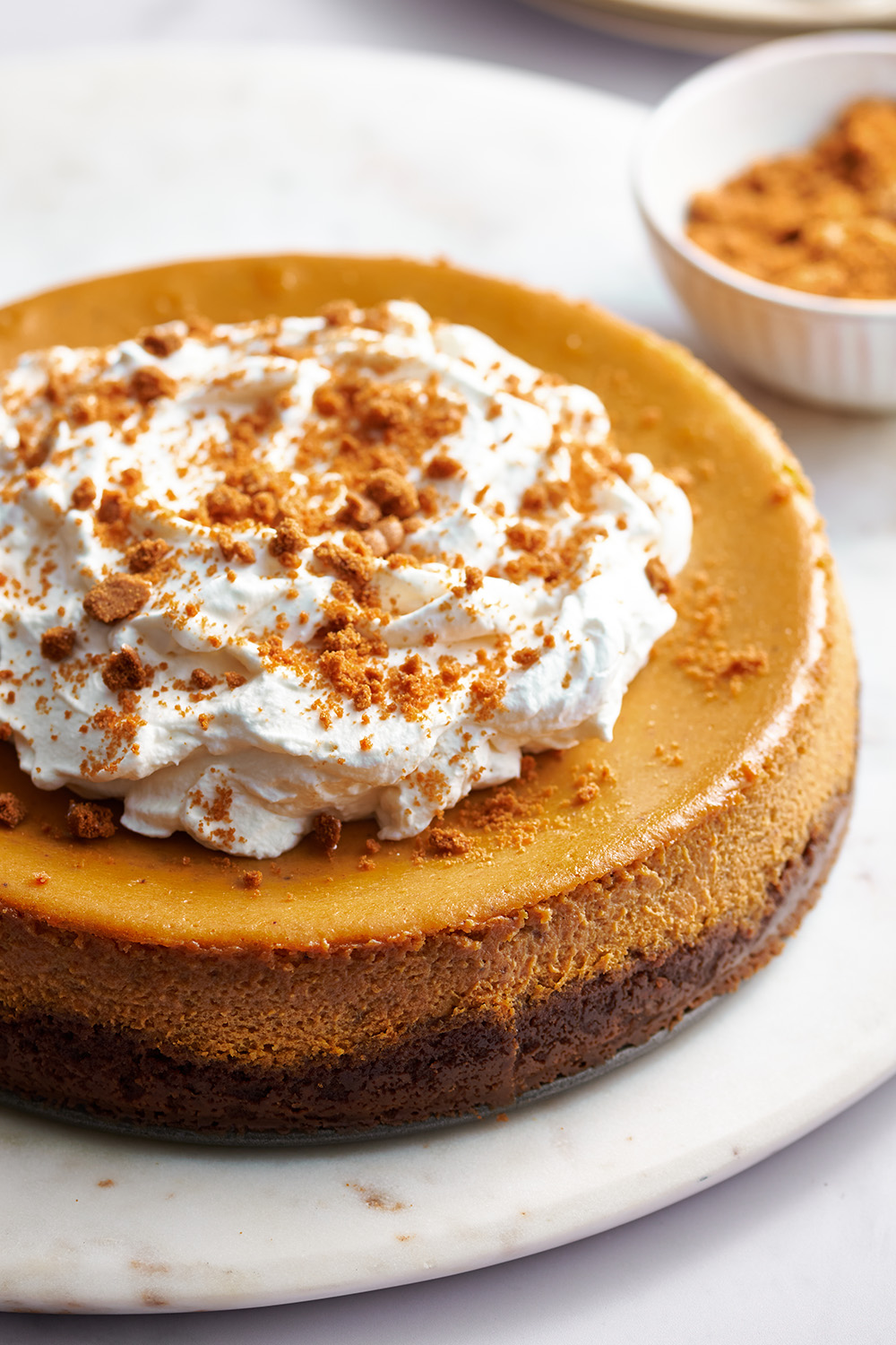 an unsliced pumpkin cheesecake, topped with whipped cream, on a table