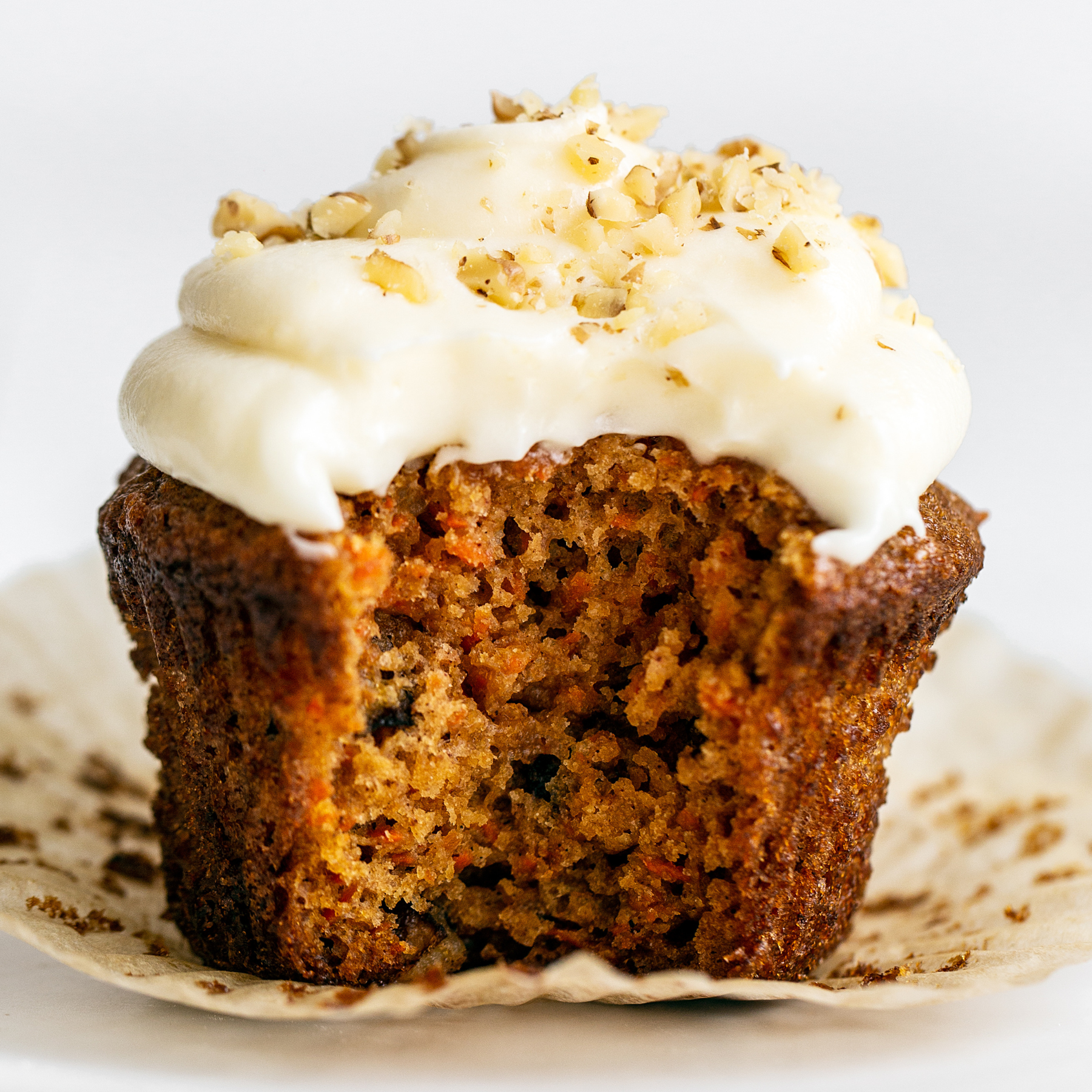 one carrot cake cupcake iced with cream cheese frosting, with its wrapper removed and a bite taken out.