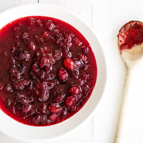 a bowl of cranberry sauce with a spoon next to it to serve.