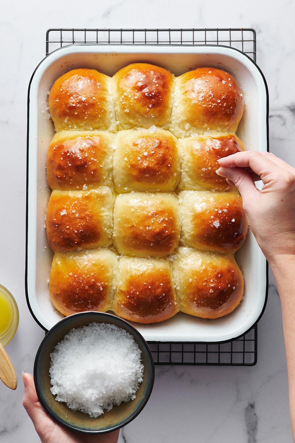 pan of baked dinner rolls being sprinkled with flaky sea salt.