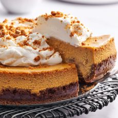 pumpkin cheesecake topped with whipped cream with a slice being removed to serve