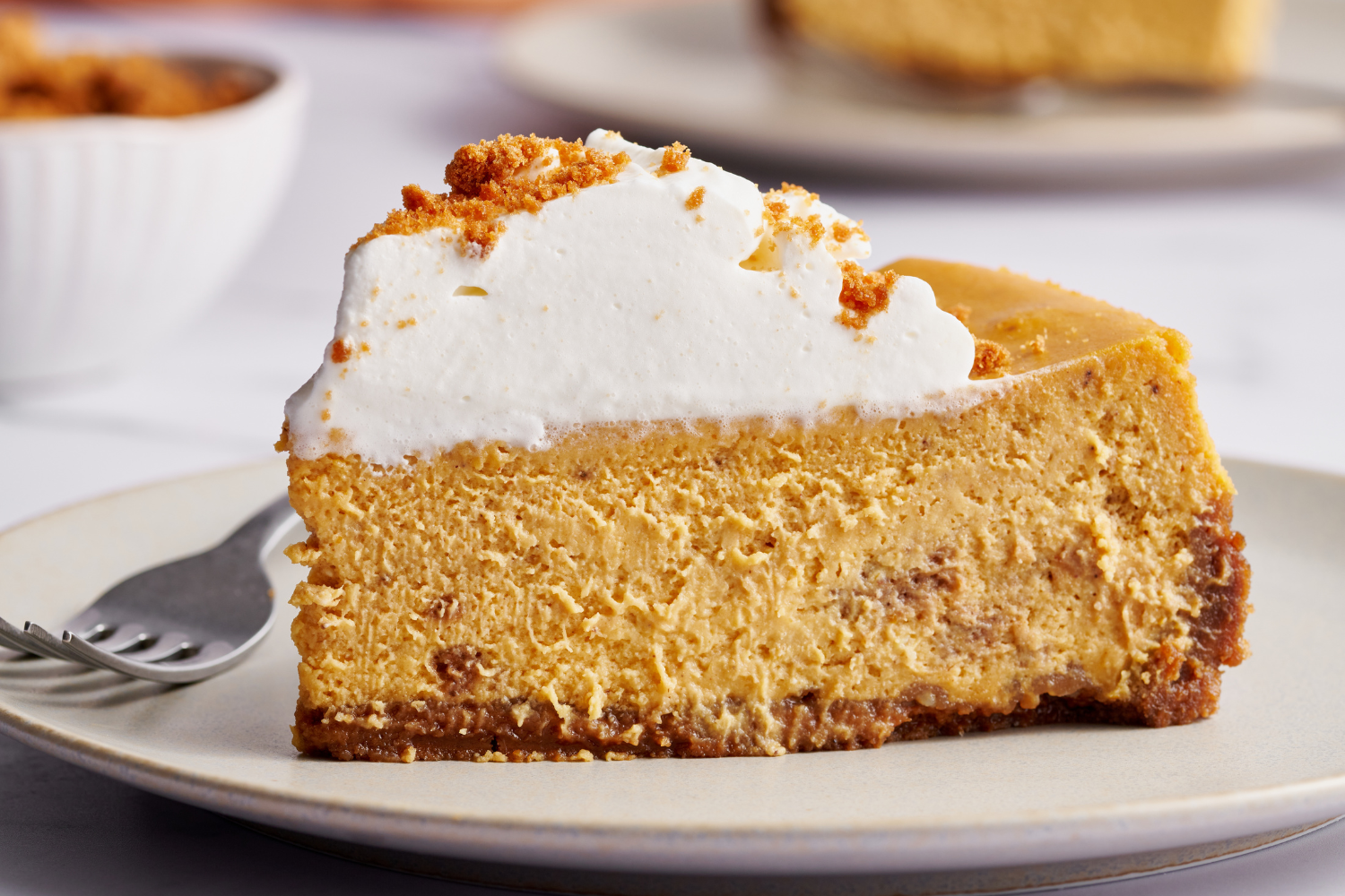 slice of pumpkin pie cheesecake, topped with whipped cream, ready to serve at Thanksgiving or any other Fall gathering!