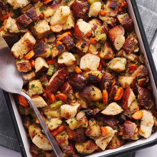 pretzel stuffing in a ceramic baking dish with a large spoon, ready to serve.