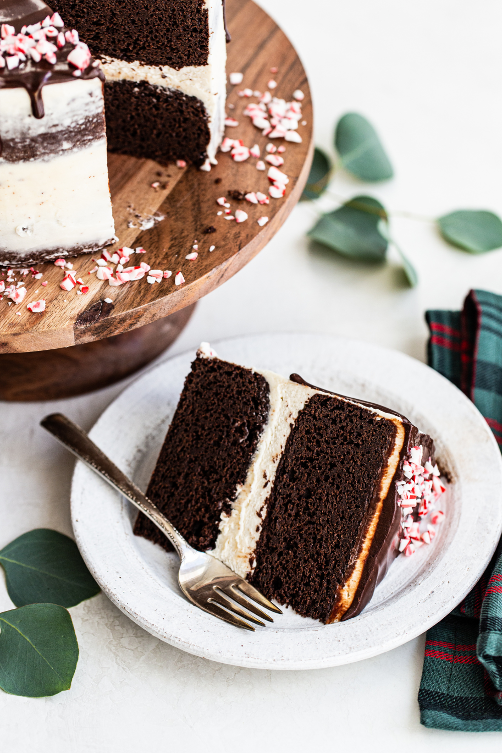 the whole Peppermint Chocolate Cake on a cake stand, with a slice of the cake on a plate, with a fork, ready to serve.