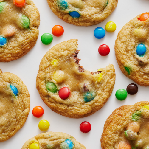several cookies on a white background, one with a bite taken out, and M&Ms scattered between.