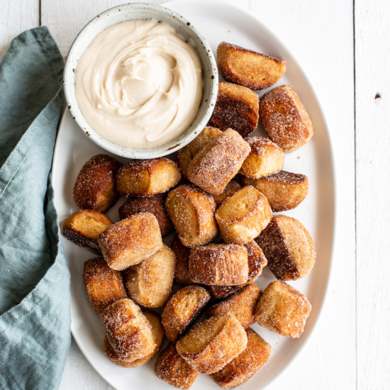 cinnamon sugar pretzel bites on a platter with a small bowl of cream cheese frosting for dipping