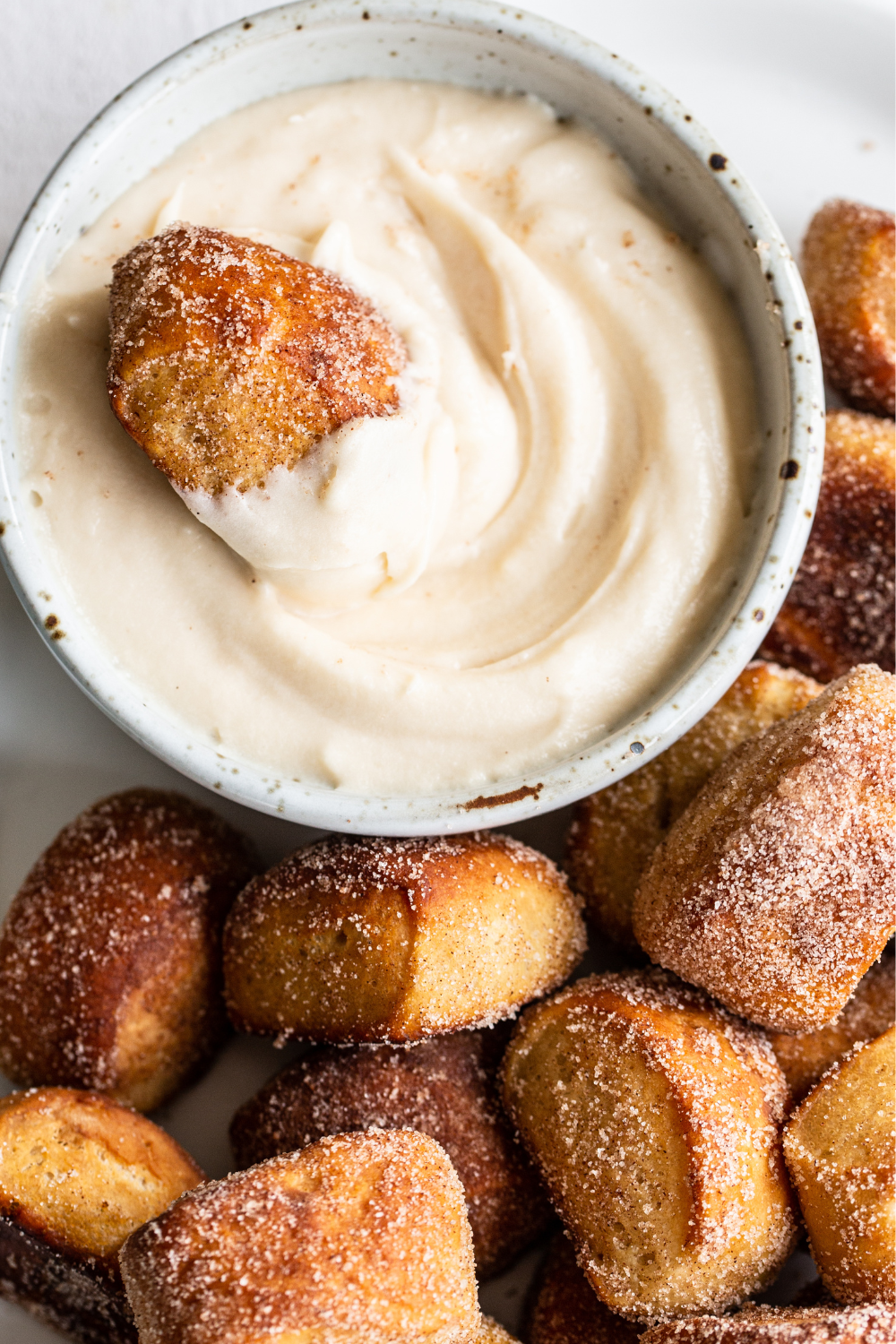 cinnamon sugar pretzel bites with a small bowl of cream cheese frosting and one pretzel bite in the frosting, dunking away