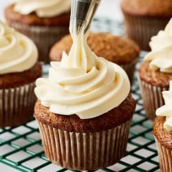 cream cheese frosting being piped on top of a carrot cake cupcake.