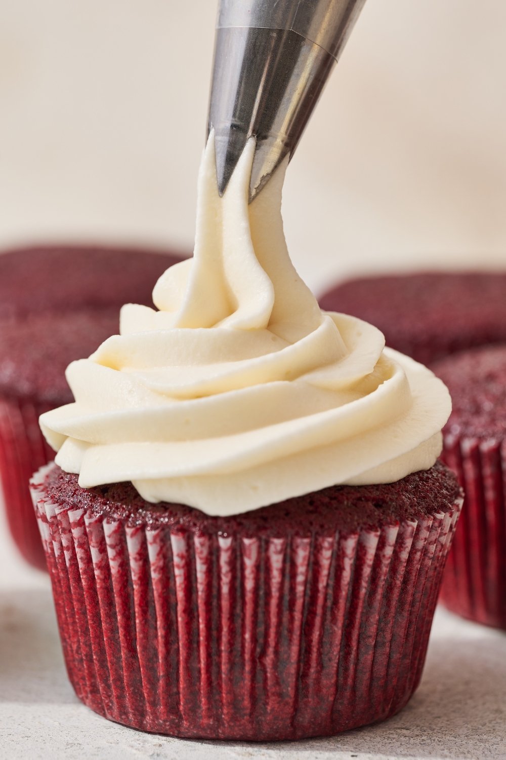 cream cheese frosting recipe being piped on top of a red velvet cupcake.