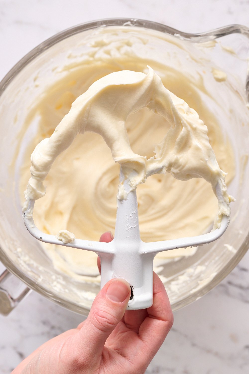 the bowl of cream cheese frosting with a beater covered in frosting.