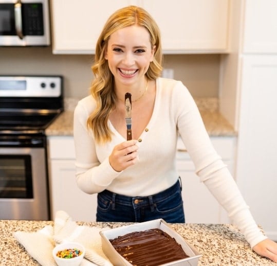 photo of Tessa wearing a white shirt and jeans, frosting a chocolate cake.