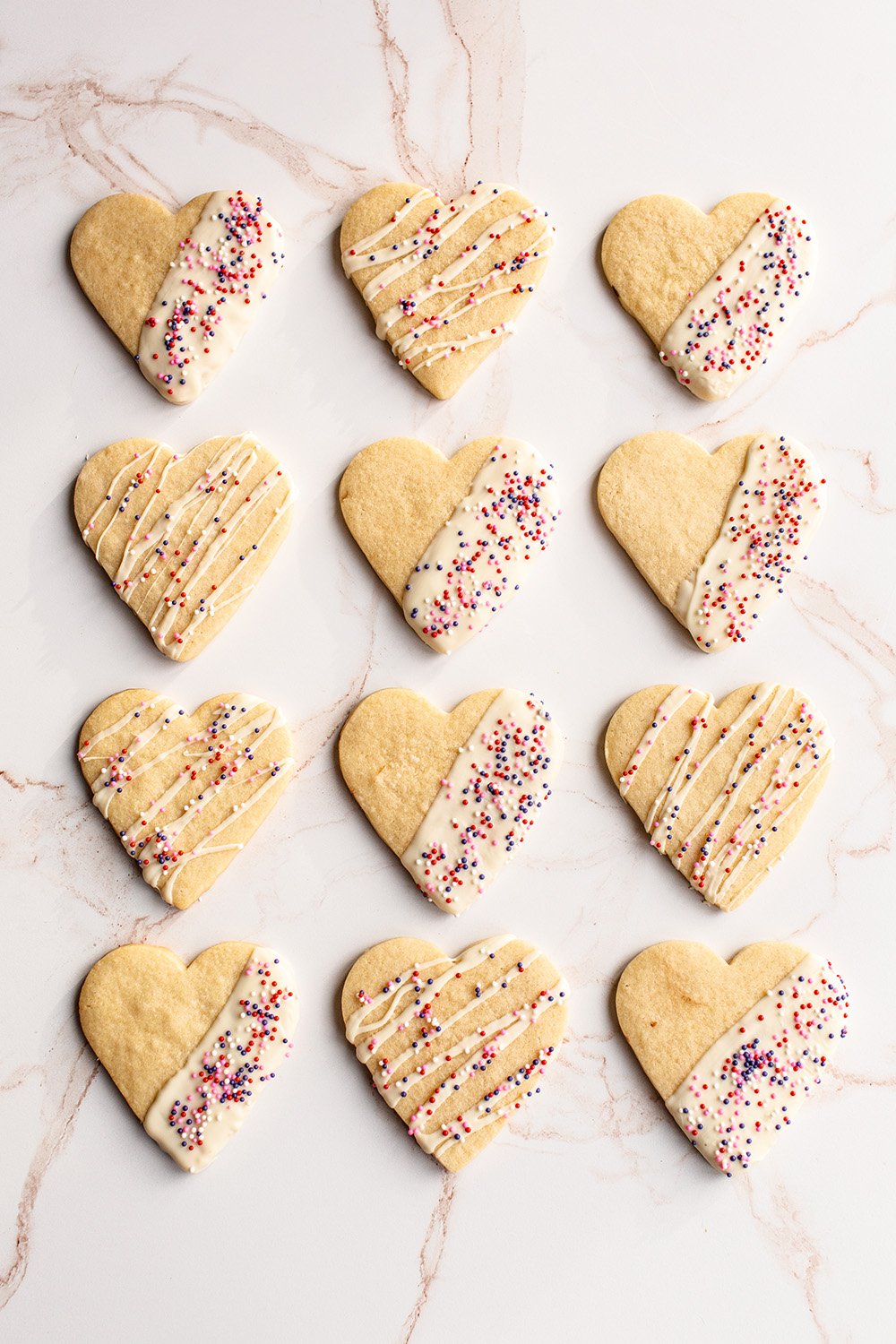 a neat row of Valentine’s Day Sugar Cookies all half dipped or drizzled with white chocolate and topped with sprinkles.