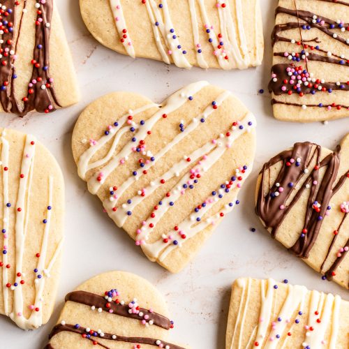 an array of heart-shaped cut-out sugar cookies all drizzled with white or dark chocolate, and finished with sprinkles.