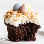 a chocolate cupcake with coconut frosting, topped with toasted coconut and chocolate eggs, with a bite taken out.