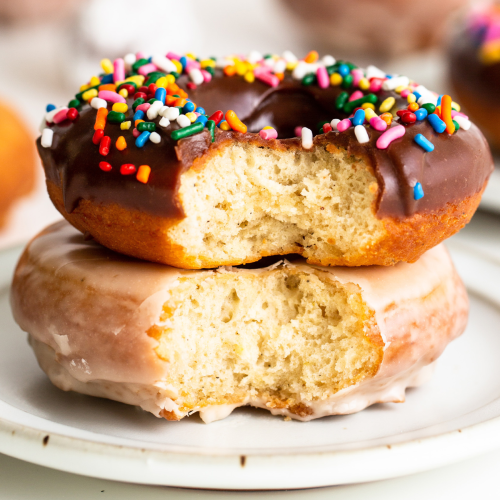 two iced cake doughnuts stacked on a plate, both with a bite taken out so you can see the fluffy interior.