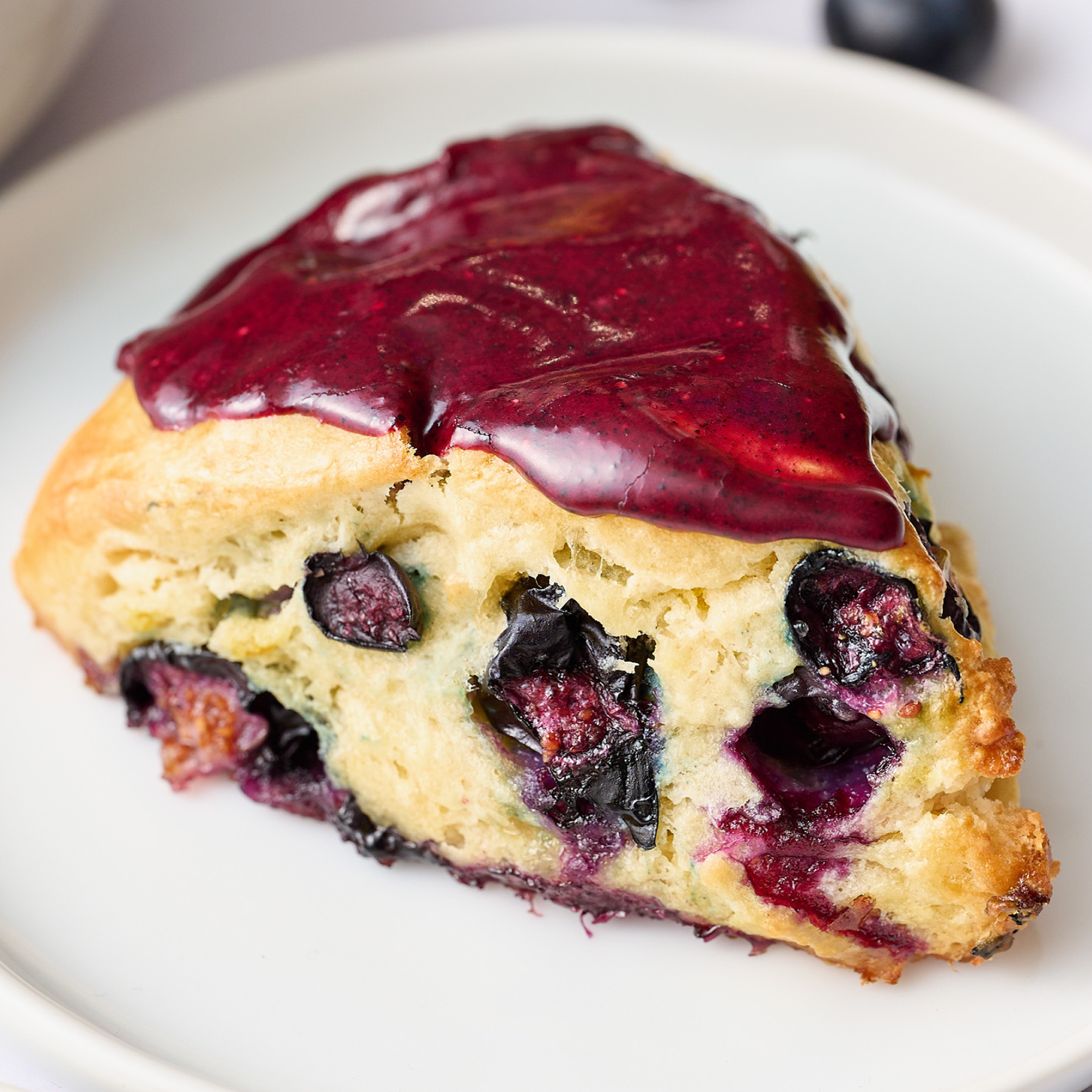 one blueberry scone with blueberry icing, on a plate, ready to serve.
