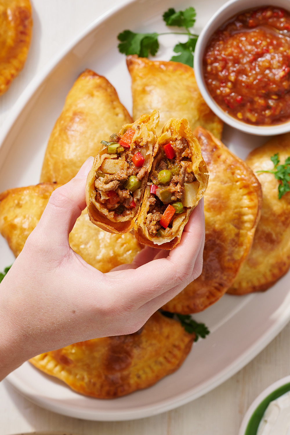 close up of a beef empanada with more underneath on a plate with some salsa for dipping