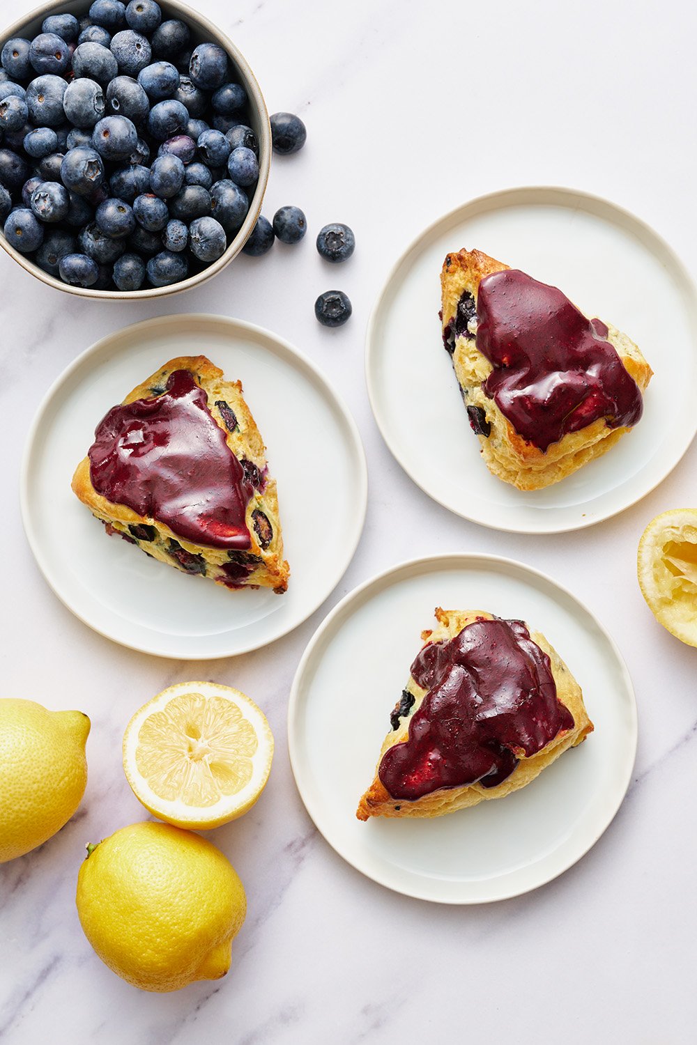 Blueberry Scones on white plates, surrounded by fresh blueberries and lemons.