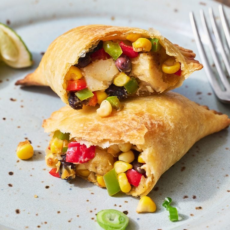 black bean, potato, pepper, corn, and spices filling of a cut open veggie empanada on a plate