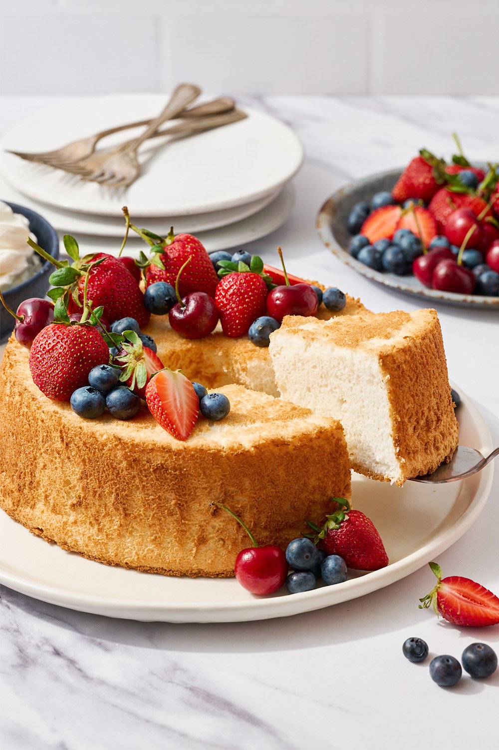 slice of angel food cake being sliced from cake, covered in fresh summer berries