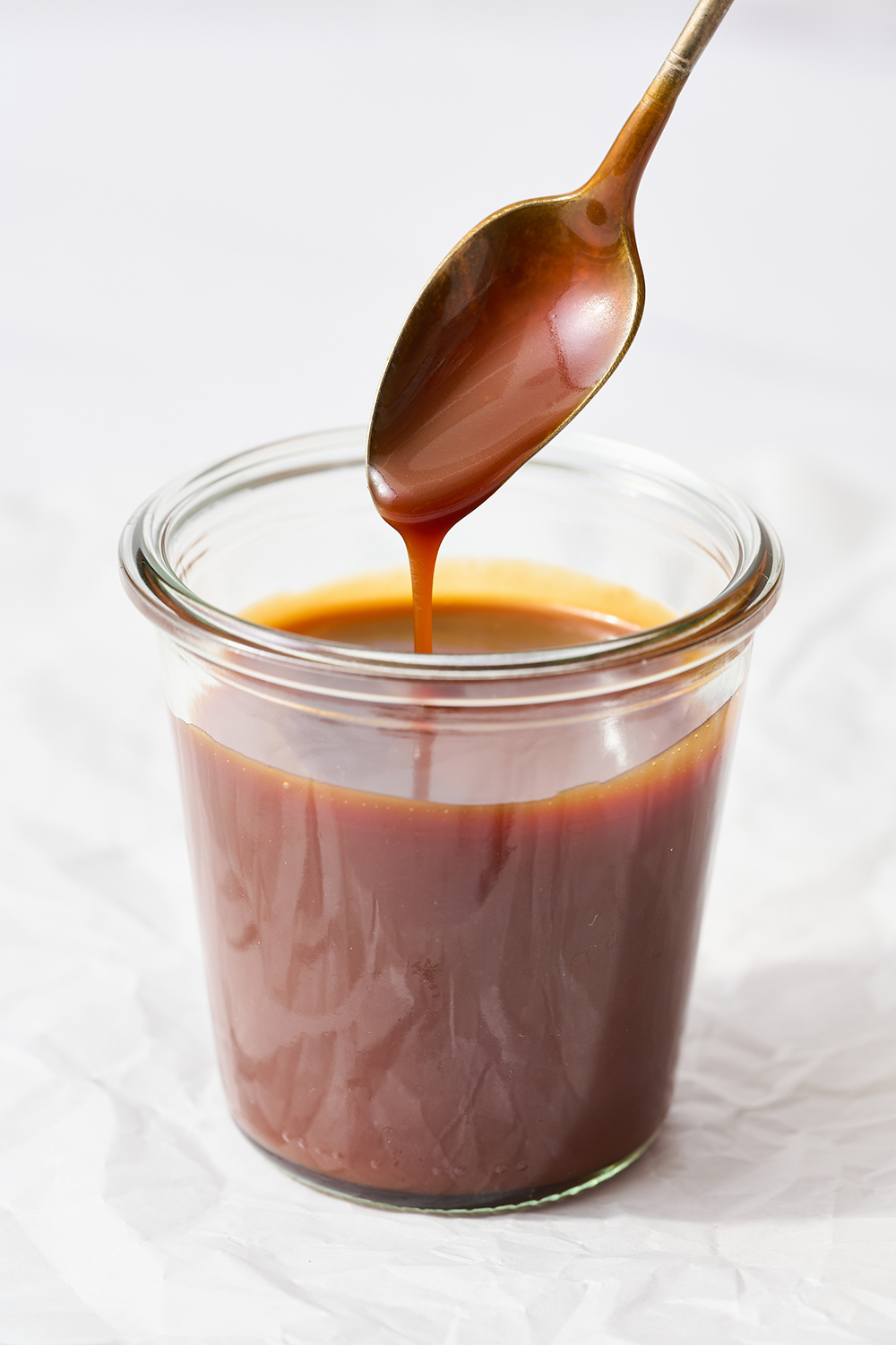 a glass jar of salted caramel, with a spoon drizzling some back into the jar.