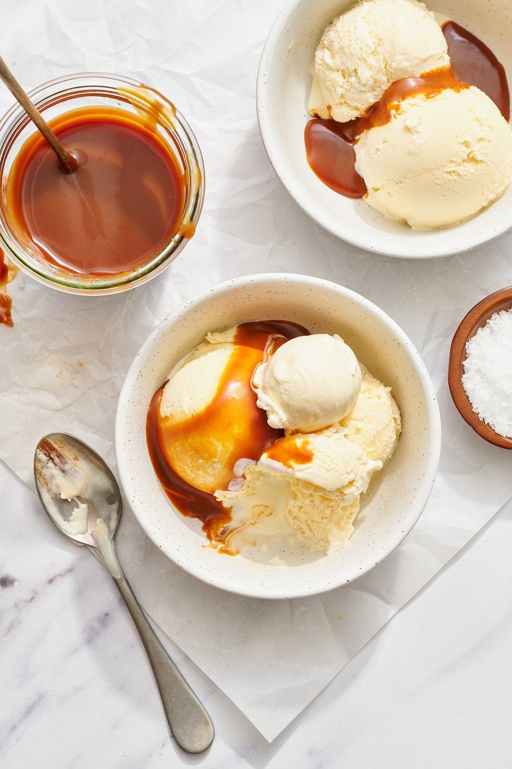small white bowls of vanilla ice cream, each drizzled with caramel sauce, and spoons nearby, ready to serve.