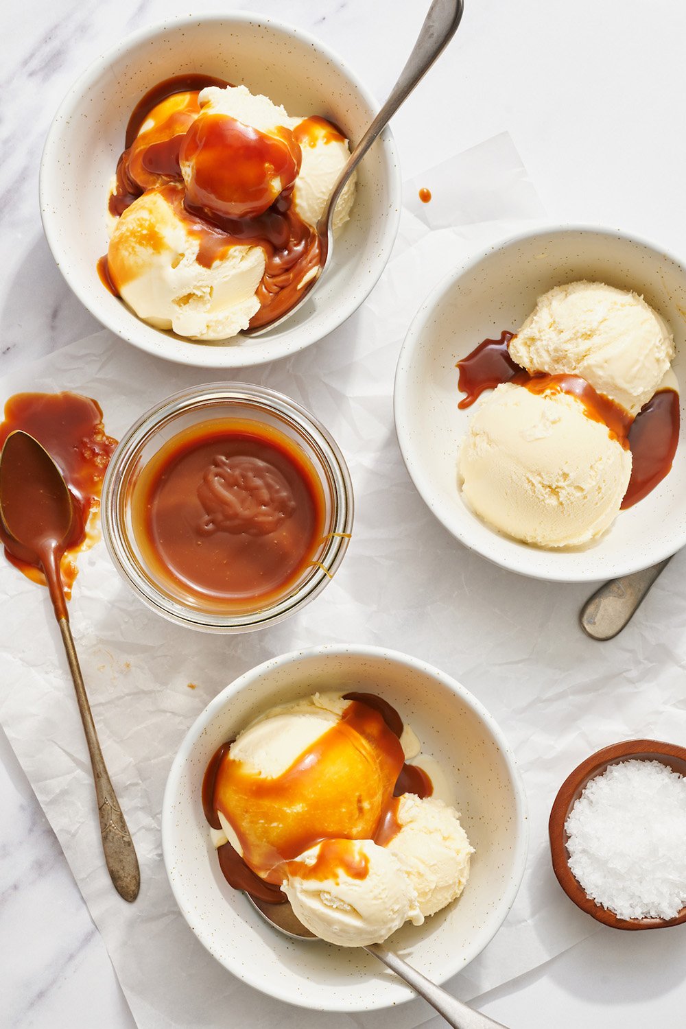 salted caramel sauce being drizzled over bowls of vanilla ice cream in bowls.
